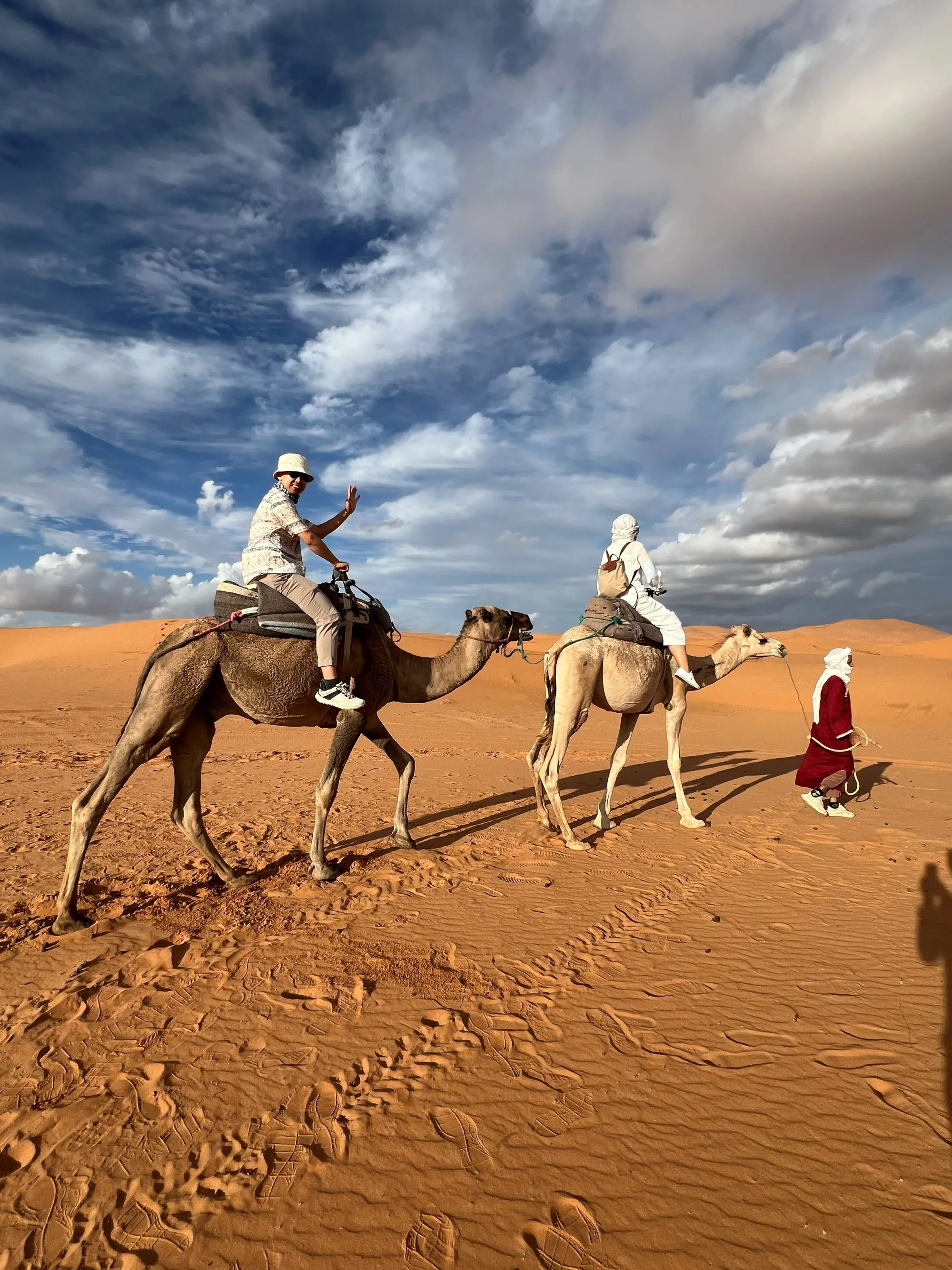 Camel riders crossing the Moroccan desert beneath a dramatic cloudy sky